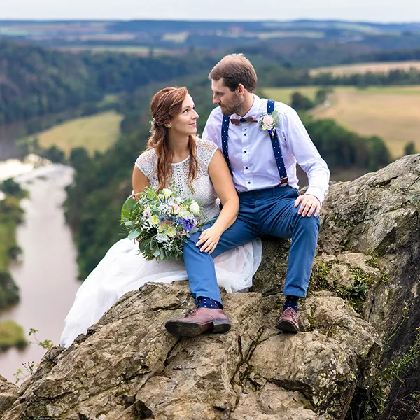 Nevěsta a ženich sedící na skále a dívající se na sebe