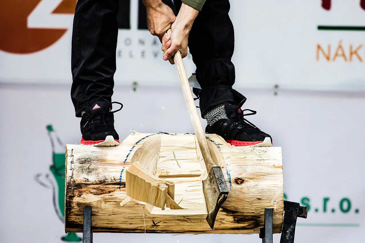 Detailní pohled na disciplínu Underhand Chop při STIHL Timbersports; sekyra dopadá do klády mezi nohy závodníka, který je chráněn speciální drátěnou ochranou obuvi.