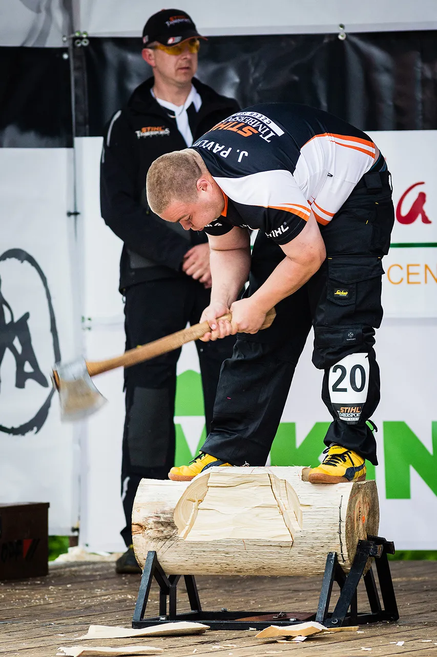 Závodník STIHL Timbersports při disciplíně Underhand Chop seká do ležící klády, na které zároveň stojí.