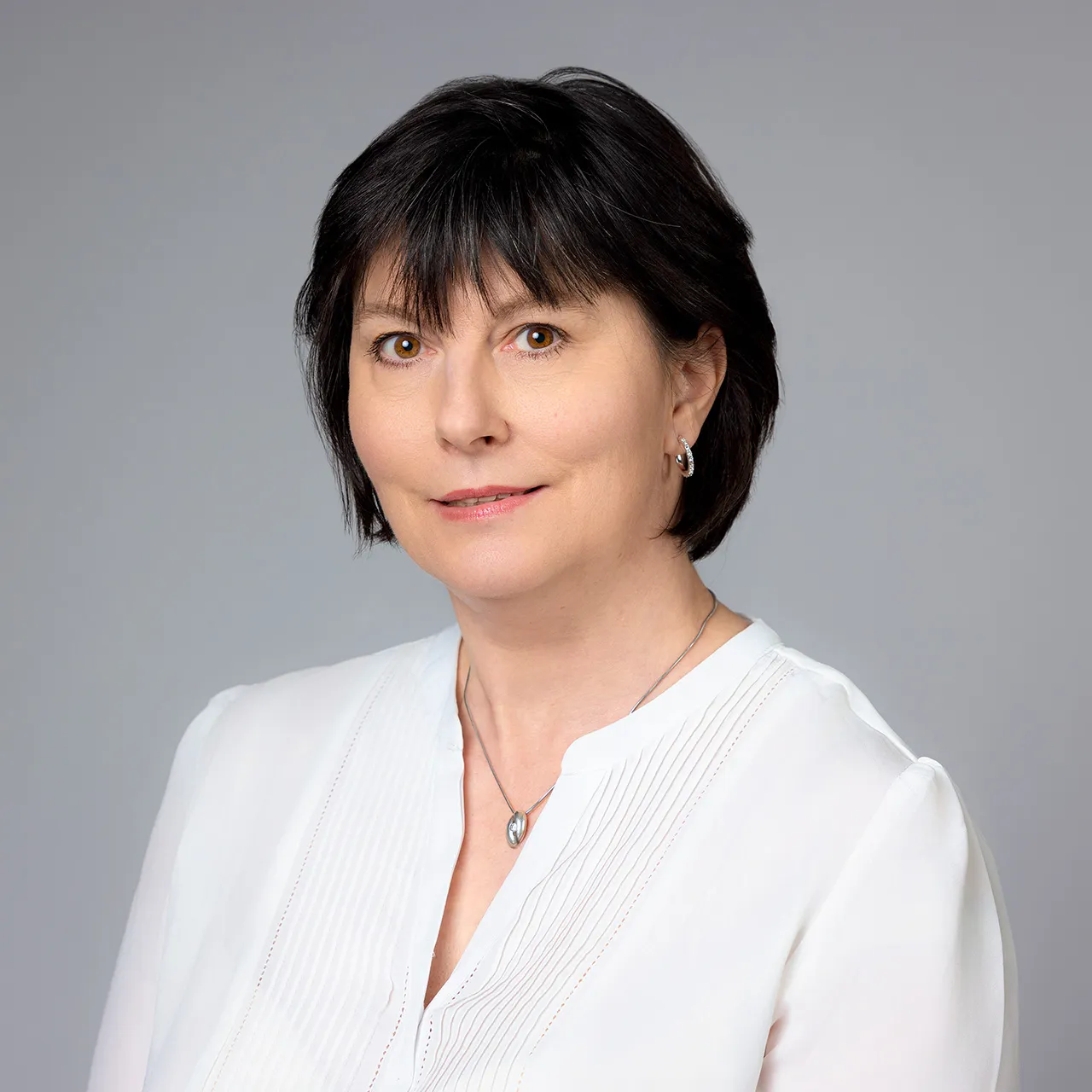 Žena v bílé halence, formální byznys portrét na šedém pozadí, čtvercový formát