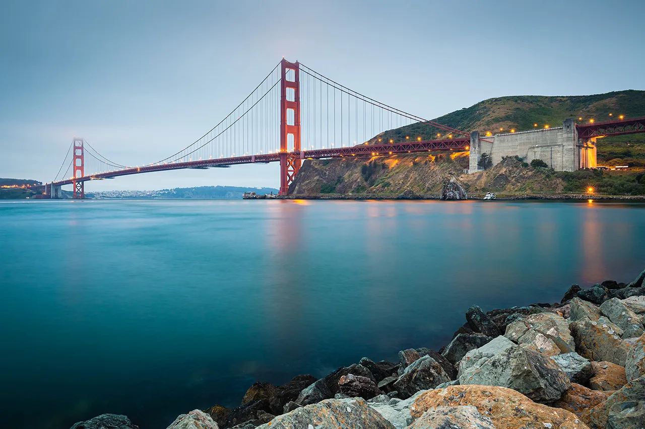 Pohled na most Golden Gate v San Franciscu přes mořskou hladinu s kamenitým pobřežím v popředí.