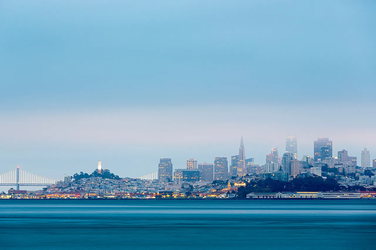 Panorama San Francisca v mlze s osvětlenými mrakodrapy a mostem Bay Bridge v pozadí.