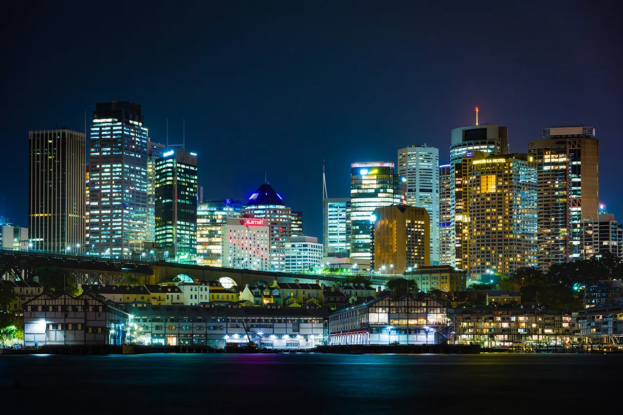 Noční panorama mrakodrapů v centru Sydney s osvětlenými budovami a přístavem.